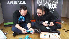 Dwóch dorosłych facetów siedzi i wypakowuje robociki Wonder Workshop